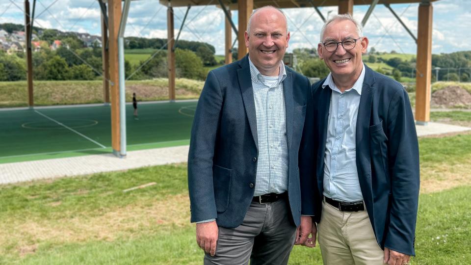 Bürgermeister André Dahlhaus und Regierungspräsident Heinrich Böckelühr vor einer überdachten Sportanlage.