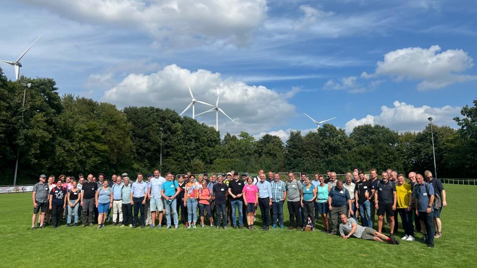 Gruppenbild vor einem Waldstück. Im Hintergrund Windkraftanlagen.