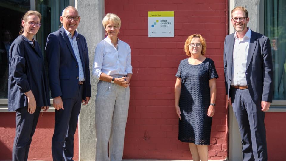 Die Personen stehen vor einem Gebäude mit der angebrachten Plakette.