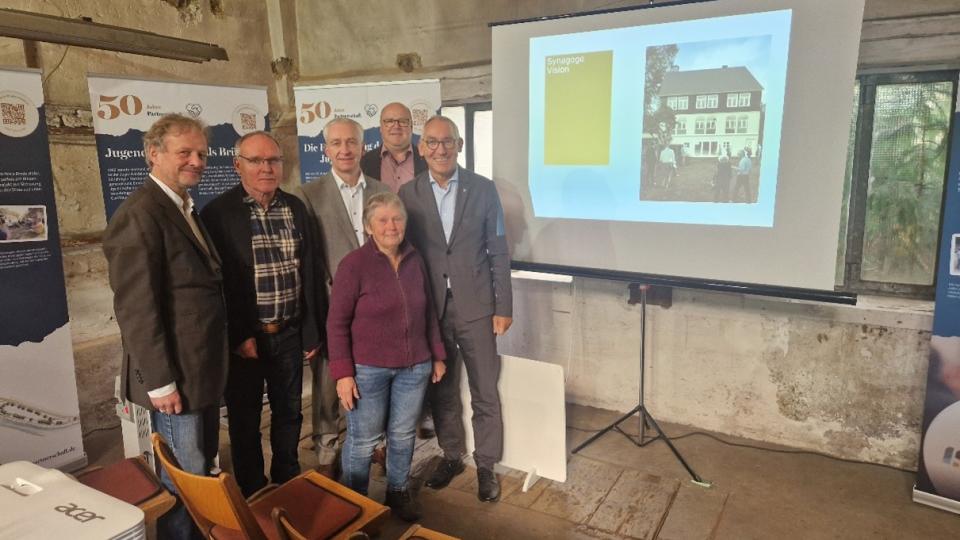 Sechs Personen stehen in einem alten Gebäude mit Informationstafeln an den Wänden