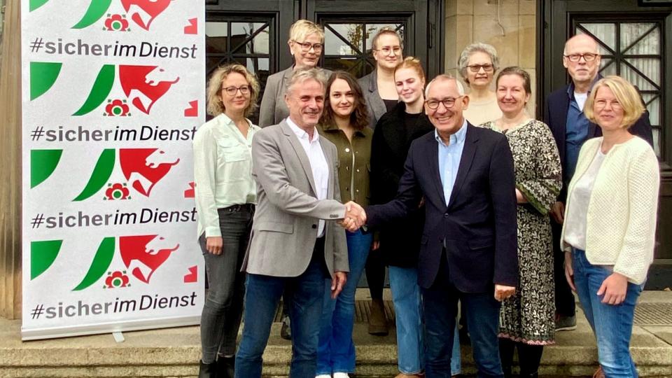 Gruppenbild mit Handschlag vor dem Slogan #sicherimDienst