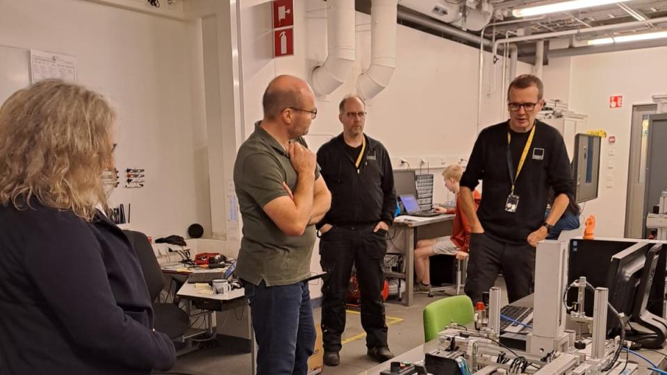 Abgebildet sind mehrere Personen, die sich in einer Technik-Werkstatt befinden.