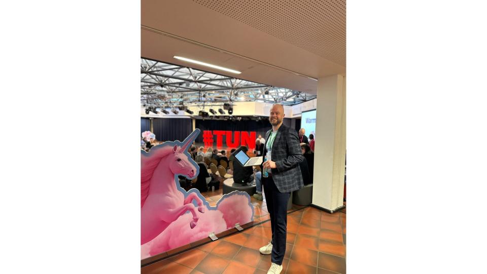 Abgebildet ist ein Mann, der sich im Rahmen der Veranstaltung #TUN24 auf einer Bühne befindet.