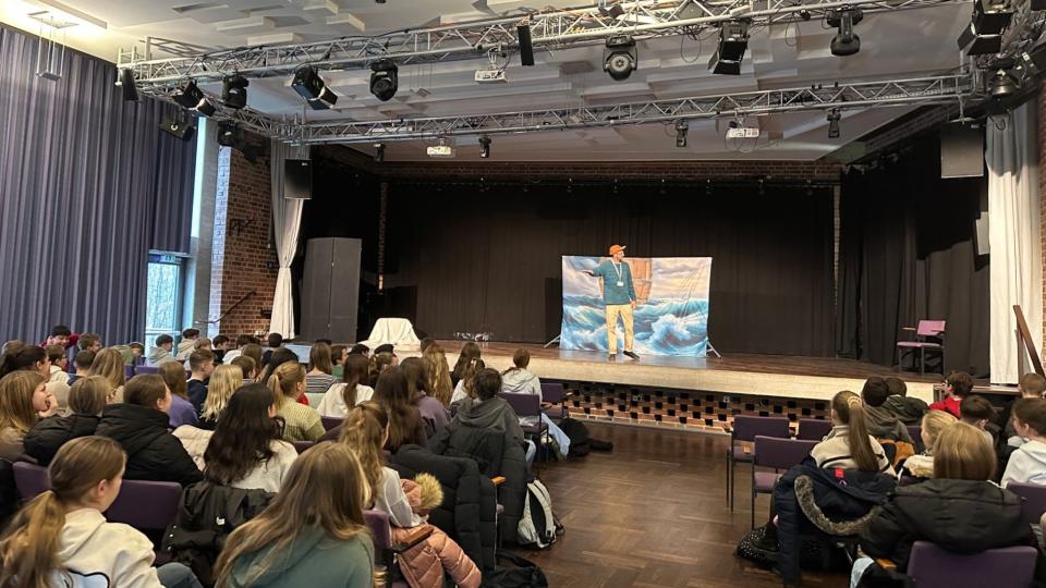 Abgebildet ist eine Theateraufführung in einer Schulaula. 