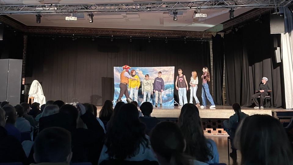 Abgebildet ist eine Theateraufführung in einer Schulaula. 