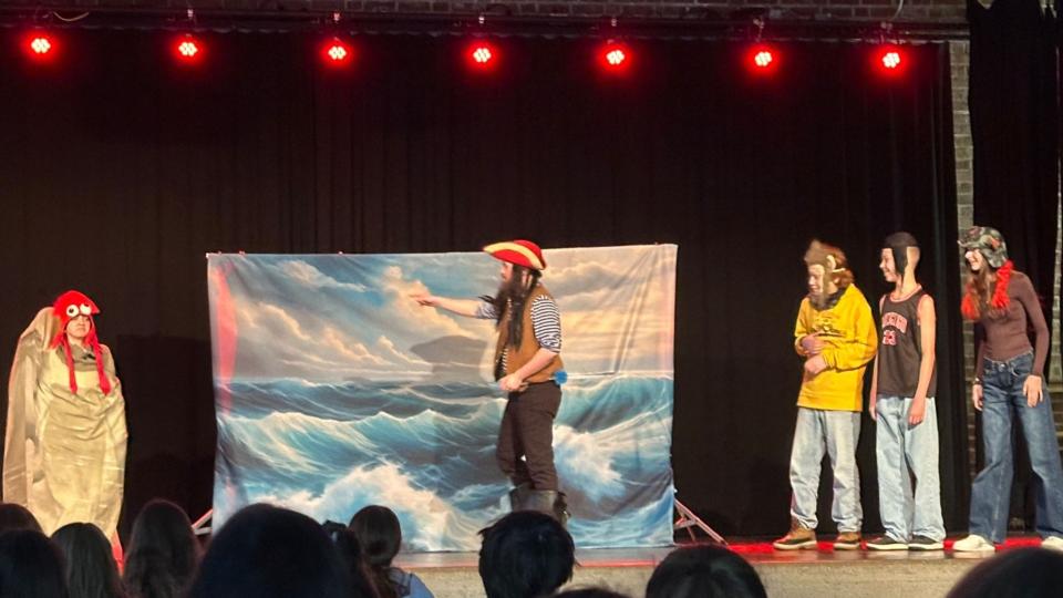 Abgebildet ist eine Theateraufführung in einer Schulaula. 