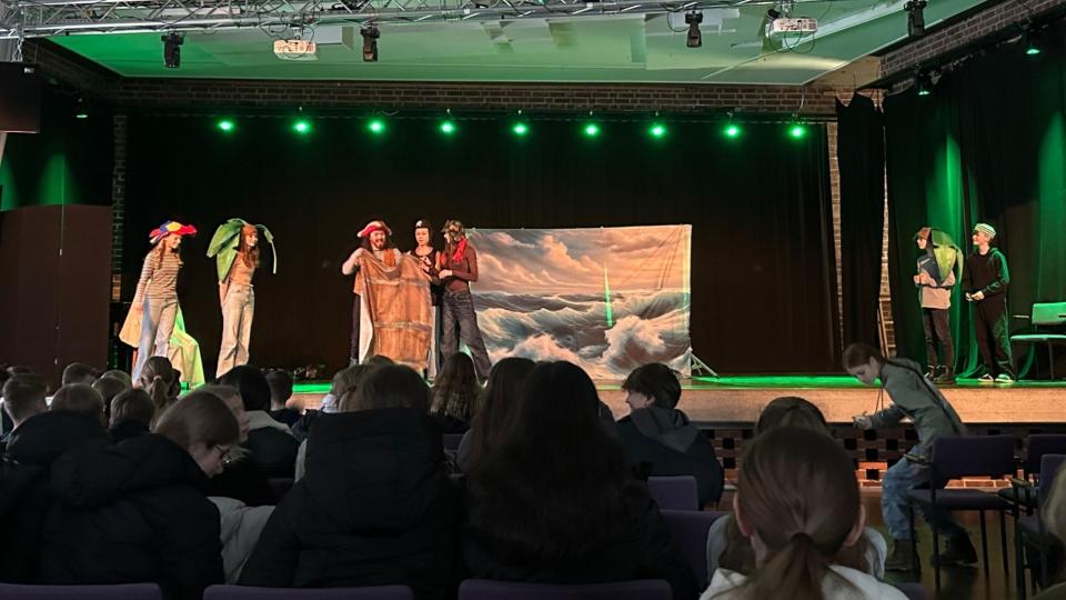 Abgebildet ist eine Theateraufführung in einer Schulaula. 