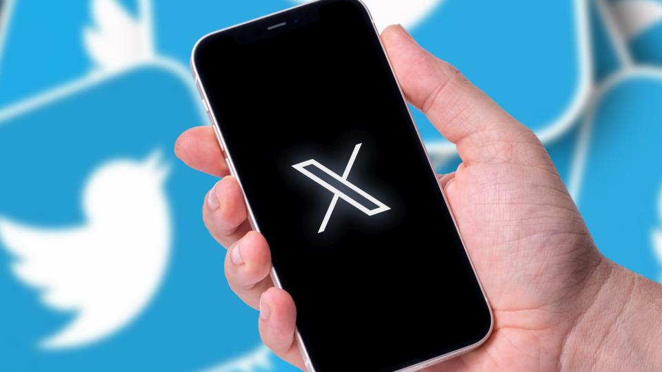 Eine Hand hält ein Smartphone auf dem das X-Logo abgebildet ist. Im Hintergrund ist das alte Twitter-Logo zu sehen.