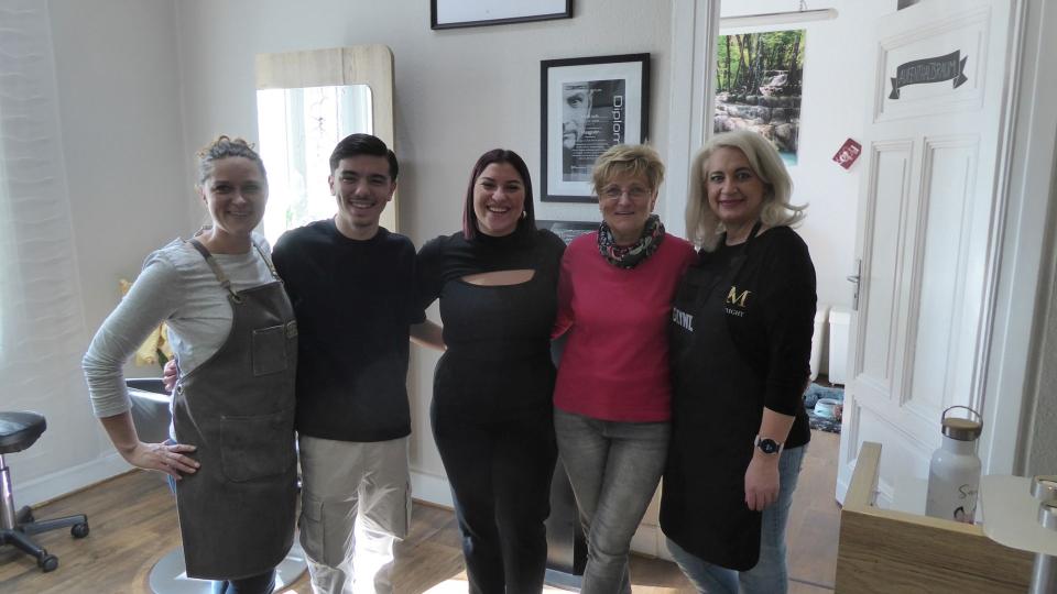 Abgebildet sind mehrere Personen, die in einem Friseursalon für ein Bild posieren.