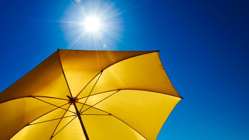 Abgebildet ist ein geöffneter gelber Sonnenschirm bei sonnigem Wetter.