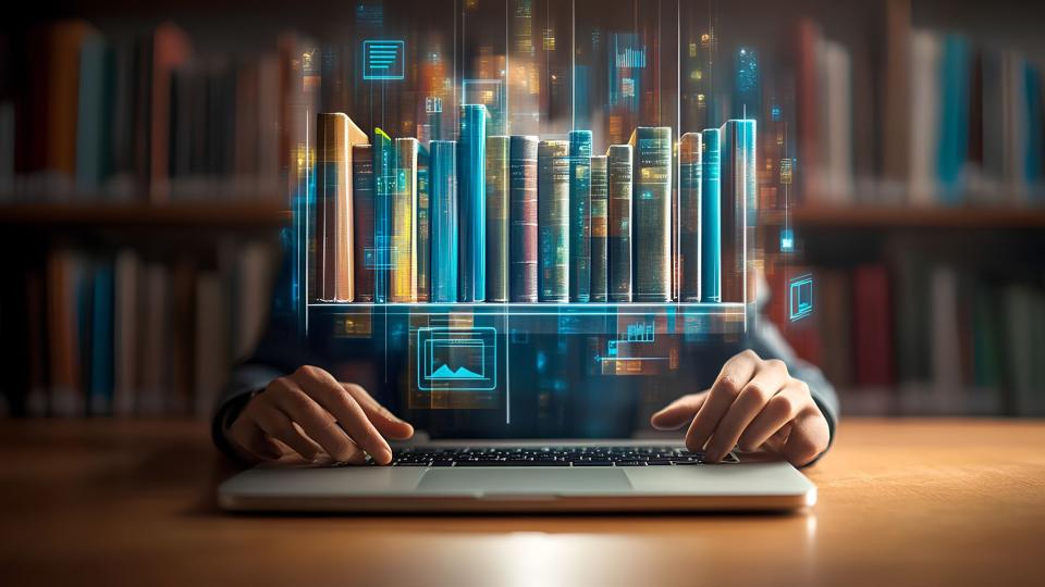 Abgebildet ist eine Person, die an einem Schreibtisch hinter einem Laptop sitzt. Der Bildschirm des Laptops ist ein Hologramm, welches Bücher in die Luft projiziert.