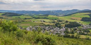 Blick von einem Hügel auf ein im Tal gelegenes Dorf.