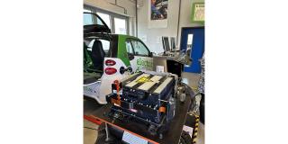 Abgebildet sind ein Elektroauto und eine ausgebaute Batterie in einer Werkstatt. 