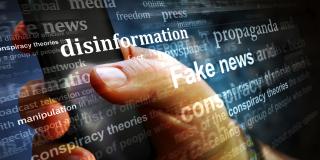 Verschiedene Begriffe zum Thema Fake News vor einer Hand die ein Smartphone hält.