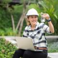 Eine Frau sitzt in einer Grünanlage und schaut auf ein mit Wasser gefülltes Reagenzglas. Sie trägt einen Schutzhelm und auf ihrem Schoß befindet sich ein Laptop.