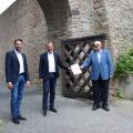 Der Siegener Stadtbaurat Henrik Schumann (l.), Bürgermeister Steffen Mues (m.) und Regierungspräsident Hans-Josef Vogel (r.) bei der Bescheid-Übergabe vor der bereits sanierten Stadt- und Schlossmauer im Bereich „Hasengarten“ 