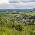 Blick von einem Hügel auf ein im Tal gelegenes Dorf.