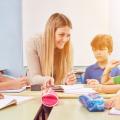 Gruppe Kinder macht zusammen mit einer Lehrerin Hausaufgaben in einer Ganztagsschule