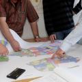 Eine Gruppe Personen beugt sich über eine Karte große Karte mit mehreren Ausschnitten.