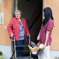 Eine Pflegerin trägt den Einkauf einer Seniorin bis zur Türschwelle ihrer Wohnung. 