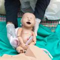 Abgebildet ist eine Übungspuppe in Form eines menschlichen Babys. Gehalten wird die Puppe von einer Person, die transparente Einweghandschuhe trägt. 