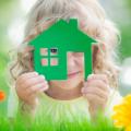 Ein kleines Mädchen hält sich die grüne Sil­hou­et­te eines Hauses vors Gesicht.