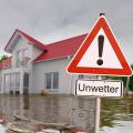 Ein Haus im Hochwasser, davor ein Hinweisschild auf die Gefahr "Unwetter".
