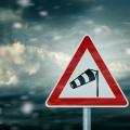 Im Vordergund ist ein Verkehrsschild mit dem Gefahrenzeichen vor starkem Seitenwind und Windböen. Im Hintergrund ist eine Wolke am Himmel zu sehen.
