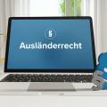 Ein aufgeklappter Laptop, auf dem Bildschirm steht Ausländerrecht. Im Hintergrund eine Waage und rechts zwei Paragraphenzeichen.