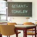 Abgebildet ist ein Klassenraum. Auf der Tafel im Klassenraum steht das Wort "Gesamtschulen".