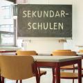 Abgebildet ist ein Klassenraum. Auf der Tafel im Klassenraum steht das Wort "Sekundarschulen".