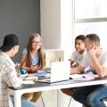 Eine Gruppe Schüler*innen sitzt um einen Tisch. Darauf liegen Bücher und ein aufgeklapptes Notebook.