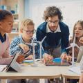 Ein Lehrer bedient ein Tablet innerhalb einer Gruppe von Schüler*innen.