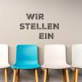 Vier Stühle, drei Weiße und einer in der Farbe Azur. Dieser ist beschriftet mit "Wir stellen ein"