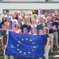 Abgebildet sind 26 Lehrerinnen und Lehrer. Zwei Personen halten eine Flagge der EU vor die gesamte Gruppe.