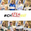 Abgebildet sind mehrere Personen, die jeweils einen Zettel mit der Aufschrift "#IchStehAuf" in die Kamera halten. 