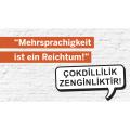 Abgebildet ist das Logo des Instituts für Turkistik der Universität Duisburg-Essen. Der Satz "Mehrsprachigkeit ist ein Reichtum!" steht sowohl auf Deutsch als auch auf Türkisch geschrieben. 