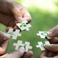 Hände reichen verschiedene Puzzelteile auf denen verschiedene Nachhaltigkeitssymbole aufgedruckt sind