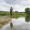 Abgebildet ist ein Angler, der an einem Fluss angelt.