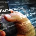 Verschiedene Begriffe zum Thema Fake News vor einer Hand die ein Smartphone hält.