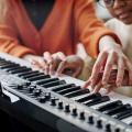 Abgebildet ist eine erwachsene Person, die einem Kind das Keyboardspielen beibringt.